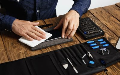 master-cleans-mobile-phone-after-successful-restoration-with-white-cloth-near-his-professional-instruments-tool-bag-wooden-table